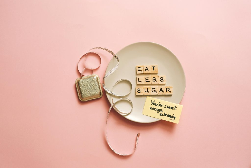Flat lay of letter tiles on plate with measuring tape, promoting health message to eat less sugar.